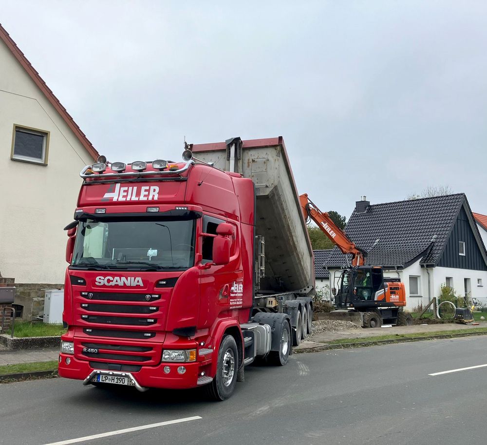 ein roter LKW entlädt Schotter und ein oranger Bagger im Hintergrund